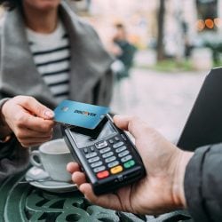 A person making a contactless credit card payment at a sidewalk café.