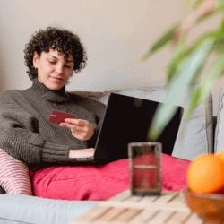 Woman sitting on a couch using a credit card to make an online purchase on a laptop at home.
