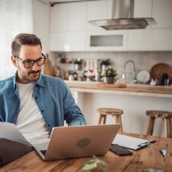 Person using a laptop and reviewing documents at a kitchen table.