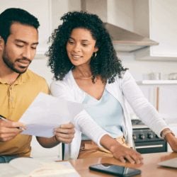 Two people discussing finances at a kitchen island while reviewing documents and using a laptop.