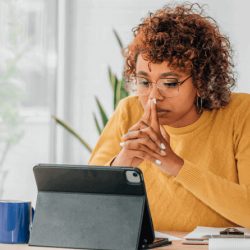 Woman in a yellow sweater focusing on a tablet at a desk.