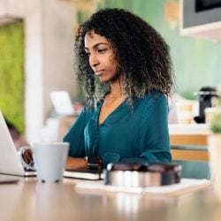 A woman works from her laptop in modern, bright, open office space.