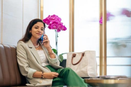 A woman sits on a couch in a waiting room talking on a mobile phone.