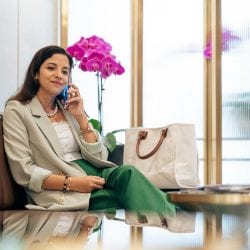 A woman sits on a couch in a waiting room talking on a mobile phone.