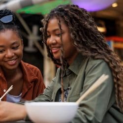 Two friends sitting in a café, one showing something on her phone to the other.