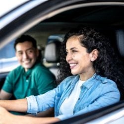 Woman driving a car with man in the passenger seat, both smiling 
