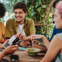 A man sits with his friends and uses his credit card at an outdoor restaurant to pay the server.