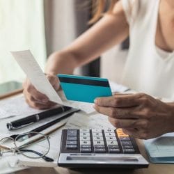 Person holding a credit card and utility bill sits at a desk with a calculator and a notebook.