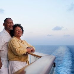 A man and woman stand together peacefully on the deck of a cruise ship admiring the sunset.