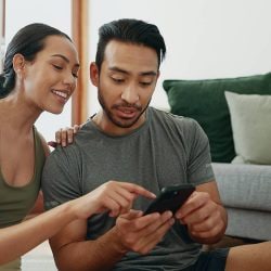 A woman explains length of credit history to her partner as they look at his credit score on his phone.