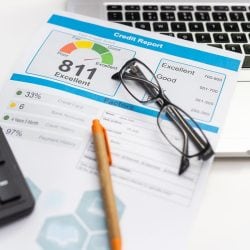 A credit report showing a person's credit rating sits next to a calculator and computer.