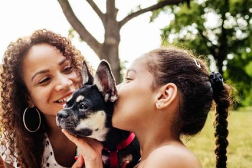 A young girl kisses her pet as her mom watches and smiles.