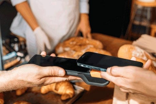Close up of a bakery employee holding a paying device while a customer makes a contactless payment transaction with their smartphone.