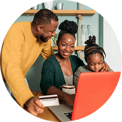 Woman types on laptop with girl sitting beside her and man holding credit card on the other side.