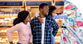 A family shops together in a supermarket. A young child reaches for a product on a shelf.