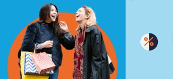 Two women laugh together as one of them holds shopping bags in her hand