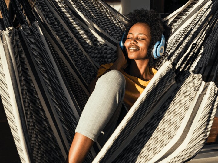 woman reclines in a large hammock while listening to music on headphones