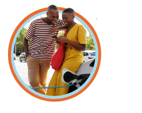 Young couple leans against car while it charges at an EV station