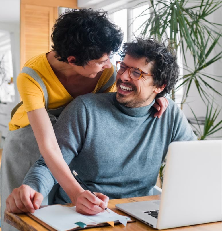 A man and woman looking at each other and smiling while looking at a laptop