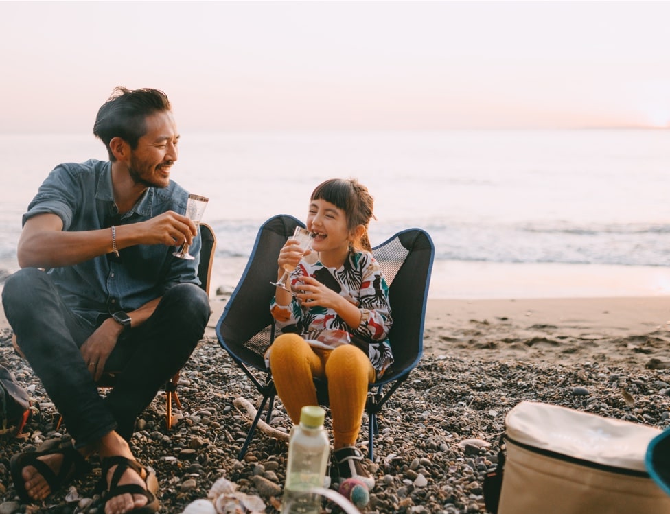 father and daughter sit together on chairs at a rocky beach