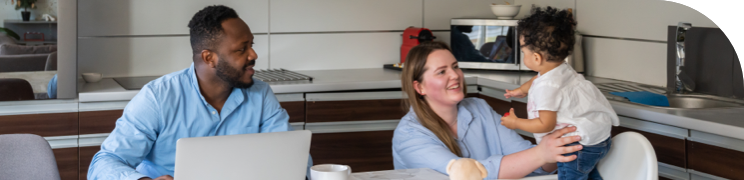 Parents sitting at a table with their young child in a modern kitchen, interacting and smiling