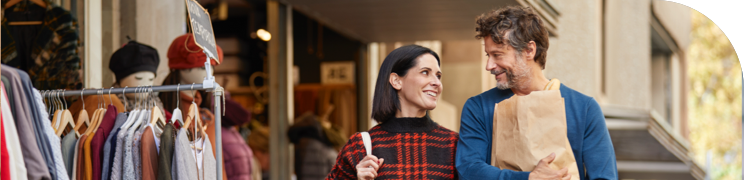 A couple smiling and walking with shopping bags outside a clothing store