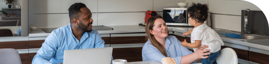 Parents sitting at a table with their young child in a modern kitchen, interacting and smiling