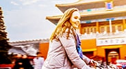 A female wearing a jacket rides a bike with an Asian-style building in the background