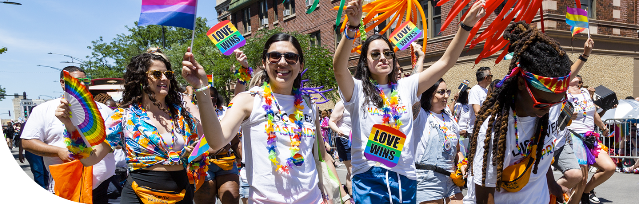 Discover employees marching in a Pride parade, holding company-branded Pride gear and signs that say "Love Wins".