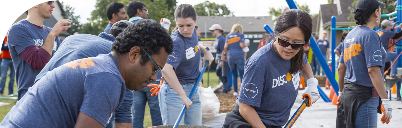 Discover employees doing an outdoor volunteer project, digging with shovels and wearing matching company tee shirts.
