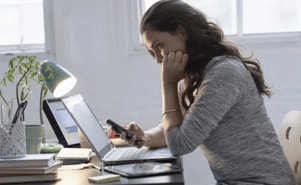 A woman using her smart phone to verify the security on a website she is accessing on her laptop.