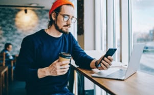 A man using his smart phone to verify the security while using his laptop in a coffee shop.