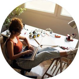 A woman sits with her feet on a table and types on a laptop computer.