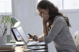 A concerned woman looking at her phone and laptop