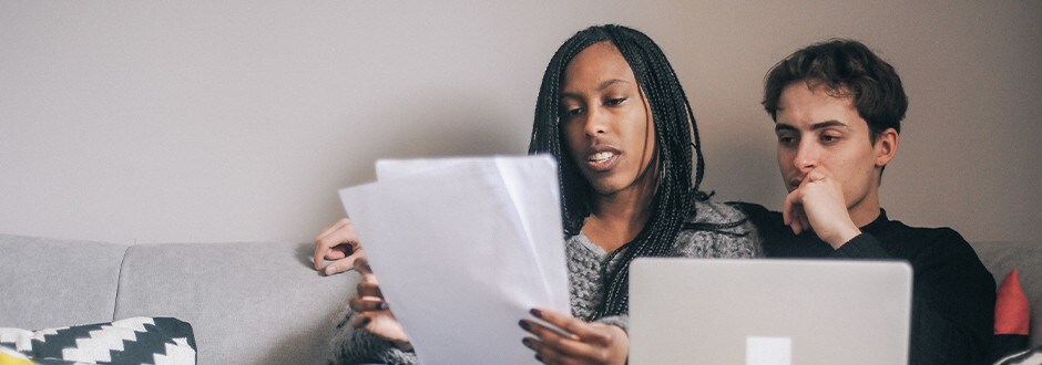 Couple sitting on the couch looking at real estate values in the neighbourhood where they are looking at purchasing a new home