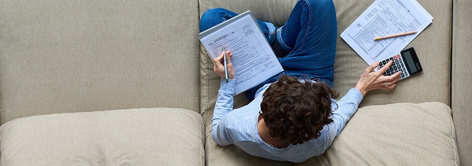 Man sitting on couch with calculator and data determining how rising interest rates may impact which loan is right