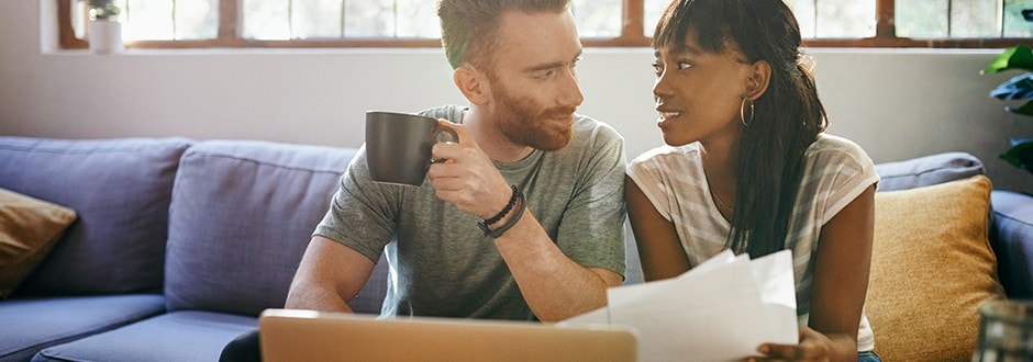 Couple sits on their couch discussing how they plan on refinancing their home and what benefits they expect 