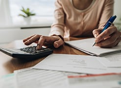 Close up of unrecognizable woman using calculator while going through bills and home finances.