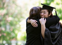Hispanic mother hugging college graduate daughter