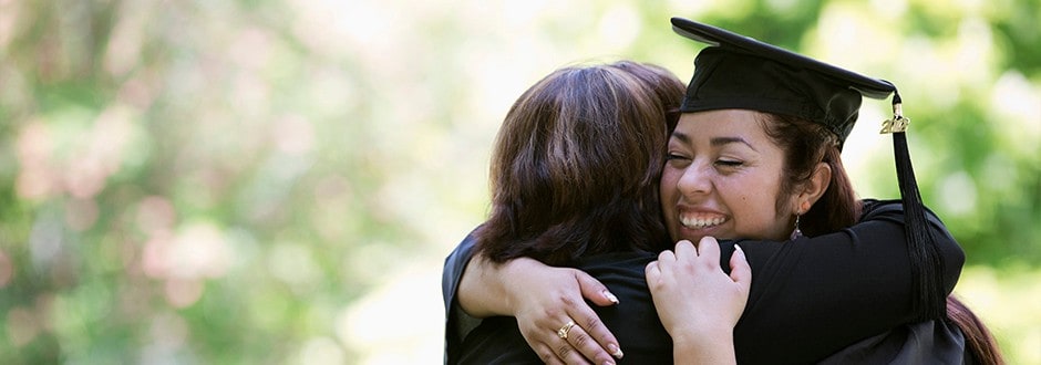 Young woman hugging her family member at her college graduation