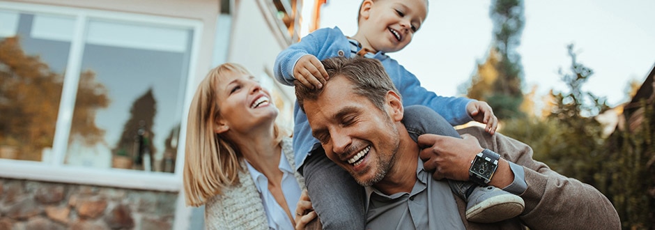 Happy family giving child a piggyback ride in front of the house they bought with home loan financing.