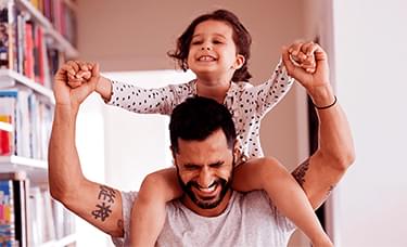 A man is holding a little girl on his shoulders in a living room.