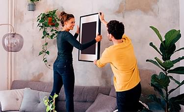 A man and woman hanging a picture frame in a living room.