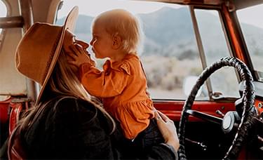 A woman kisses her child in the front seat of a truck.