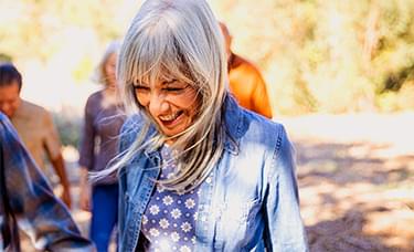 A retired woman smiling and walking through the woods with people.