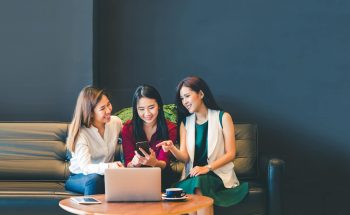 Three women look at a smartphone.
