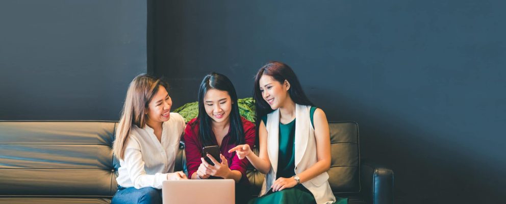 Three women look at a smartphone.