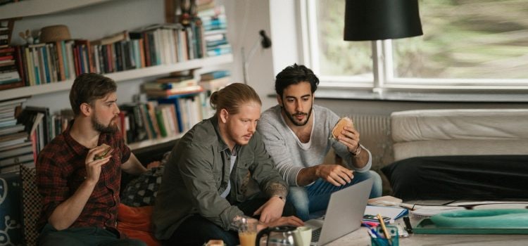 Three college students eating sandwiches while working on a group project