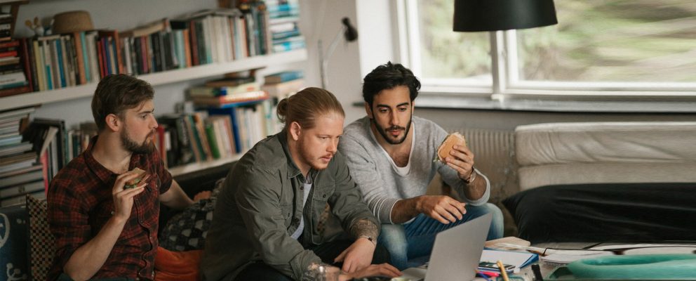 Three college students eating sandwiches while working on a group project