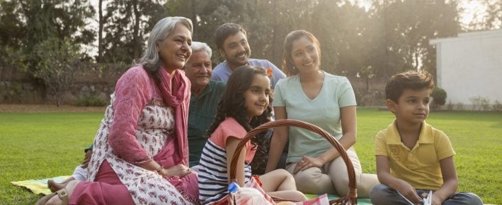 A family of four, with the children's grandmother and grandfather, enjoy a picnic in the park.